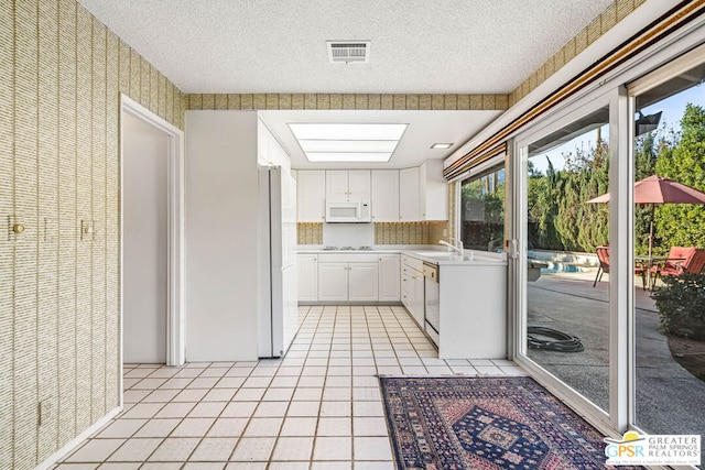 kitchen featuring a textured ceiling, light tile patterned floors, white cabinets, and white appliances