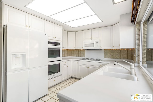 kitchen with white appliances, white cabinets, sink, kitchen peninsula, and light tile patterned floors