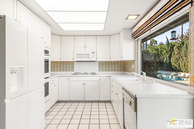 kitchen featuring decorative backsplash, sink, white appliances, light tile patterned floors, and white cabinets