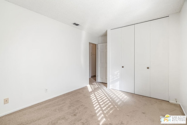 unfurnished bedroom featuring a textured ceiling, a closet, and light carpet