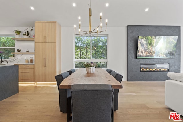 dining area with a fireplace, sink, a chandelier, and light hardwood / wood-style flooring