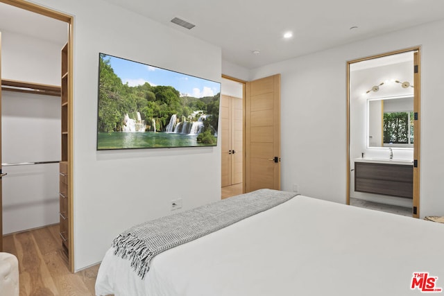 bedroom with light hardwood / wood-style floors, a walk in closet, a closet, and ensuite bath