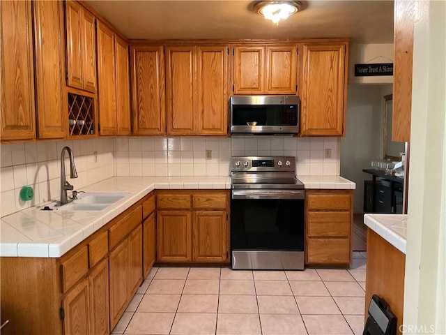 kitchen with light tile patterned floors, tile countertops, stainless steel appliances, backsplash, and sink