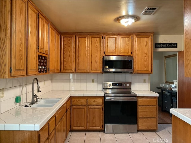 kitchen with tasteful backsplash, tile countertops, sink, light tile patterned flooring, and appliances with stainless steel finishes