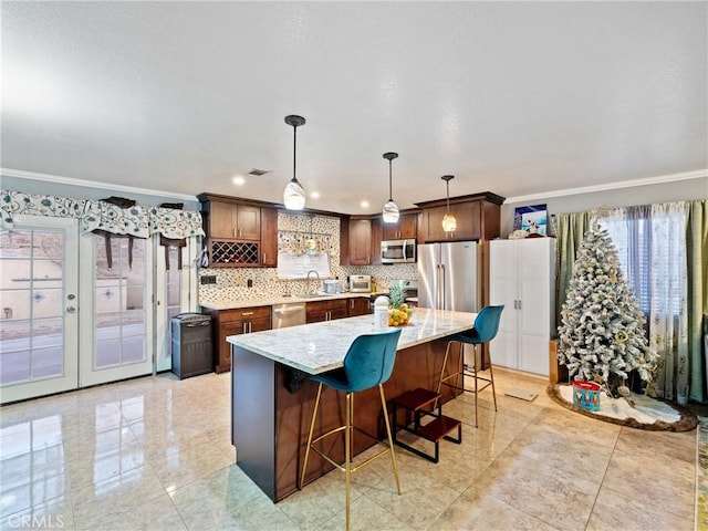 kitchen featuring decorative light fixtures, backsplash, a kitchen island, ornamental molding, and stainless steel appliances