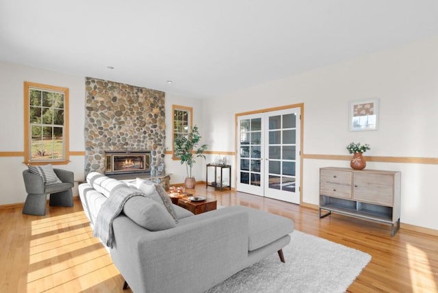 living room with hardwood / wood-style flooring, a stone fireplace, french doors, and a wealth of natural light