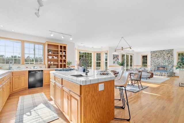 kitchen featuring sink, tile countertops, a center island with sink, a kitchen breakfast bar, and black dishwasher