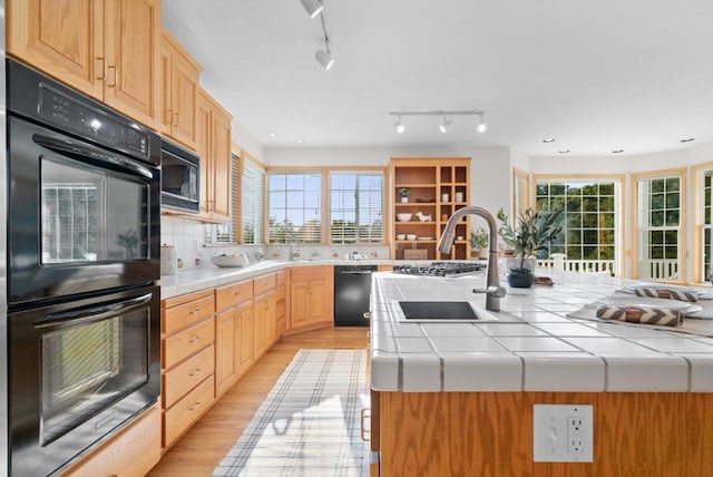 kitchen with light hardwood / wood-style flooring, tile counters, black appliances, a kitchen island, and light brown cabinets