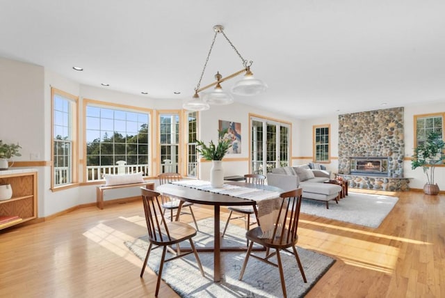 dining area featuring a stone fireplace, plenty of natural light, and light wood-type flooring