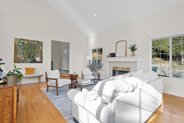 living room featuring high vaulted ceiling, a tile fireplace, and light hardwood / wood-style flooring