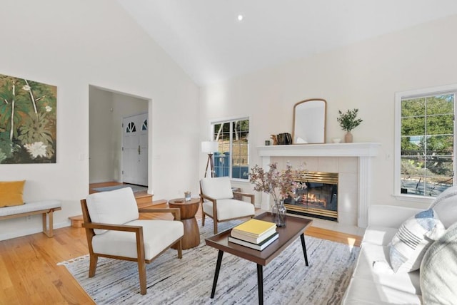 living room with high vaulted ceiling, a fireplace, and light hardwood / wood-style floors