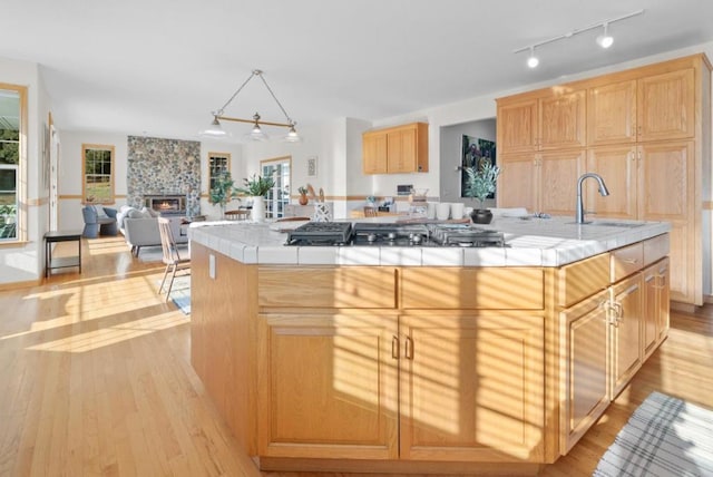 kitchen featuring a center island, a fireplace, tile counters, stainless steel gas cooktop, and light wood-type flooring