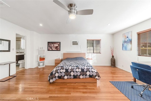 bedroom featuring ceiling fan, a wall mounted air conditioner, connected bathroom, and light hardwood / wood-style floors