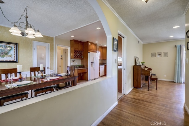 dining room featuring a textured ceiling, crown molding, hardwood / wood-style floors, and an inviting chandelier