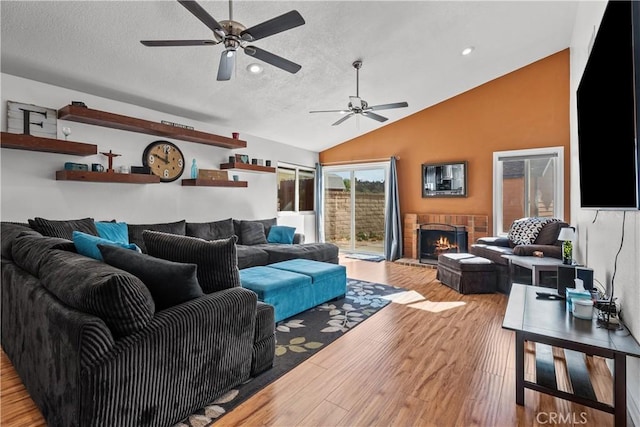 living room featuring ceiling fan, vaulted ceiling, a brick fireplace, light hardwood / wood-style floors, and a textured ceiling