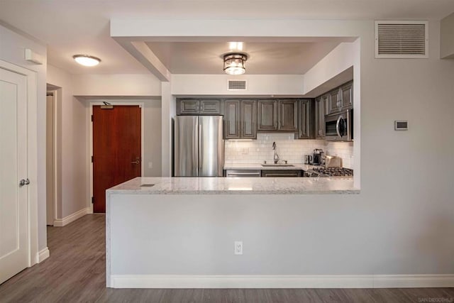 kitchen with hardwood / wood-style floors, appliances with stainless steel finishes, decorative backsplash, light stone counters, and sink