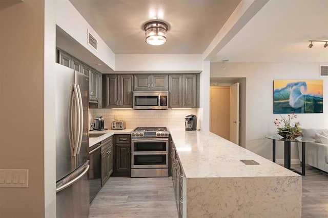 kitchen featuring light hardwood / wood-style floors, kitchen peninsula, decorative backsplash, light stone countertops, and appliances with stainless steel finishes