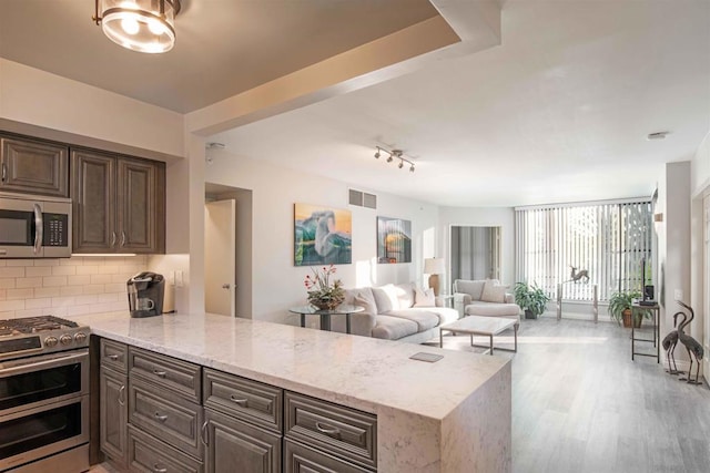 kitchen featuring light stone countertops, kitchen peninsula, appliances with stainless steel finishes, and dark brown cabinetry