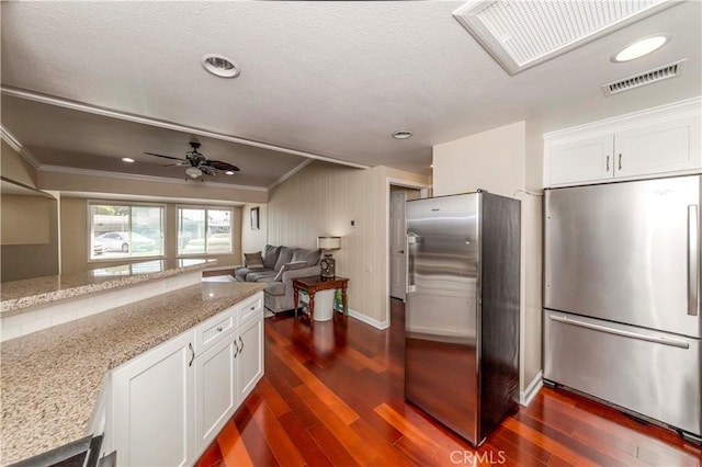 kitchen with light stone countertops, stainless steel refrigerator, and white cabinetry