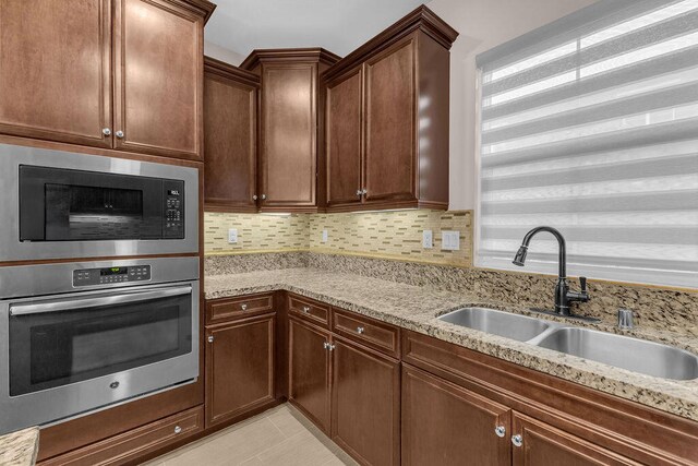 kitchen with decorative backsplash, sink, stainless steel oven, light stone counters, and built in microwave