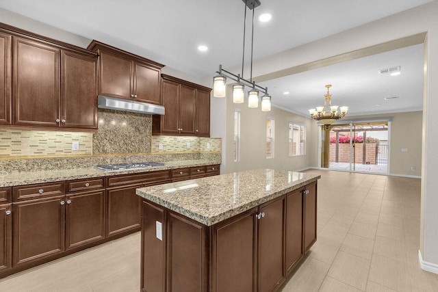 kitchen featuring decorative light fixtures, light stone counters, stainless steel gas stovetop, and an inviting chandelier