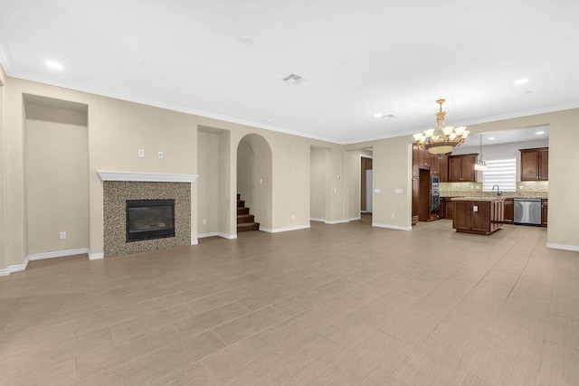 unfurnished living room featuring sink, a tile fireplace, crown molding, and an inviting chandelier