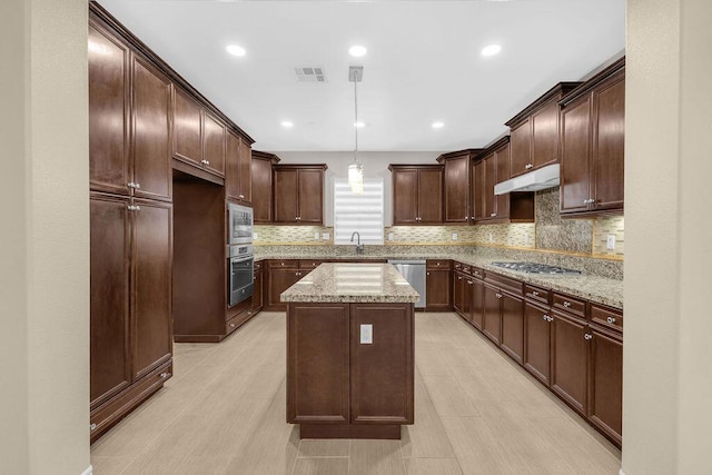 kitchen with appliances with stainless steel finishes, light stone countertops, a kitchen island, pendant lighting, and dark brown cabinetry