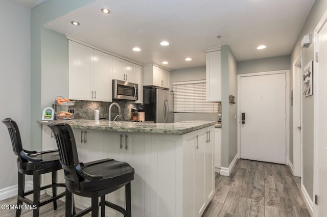 kitchen with white cabinetry, appliances with stainless steel finishes, kitchen peninsula, and light stone countertops