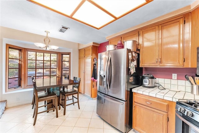 kitchen with stainless steel appliances, an inviting chandelier, light tile patterned flooring, tile counters, and hanging light fixtures