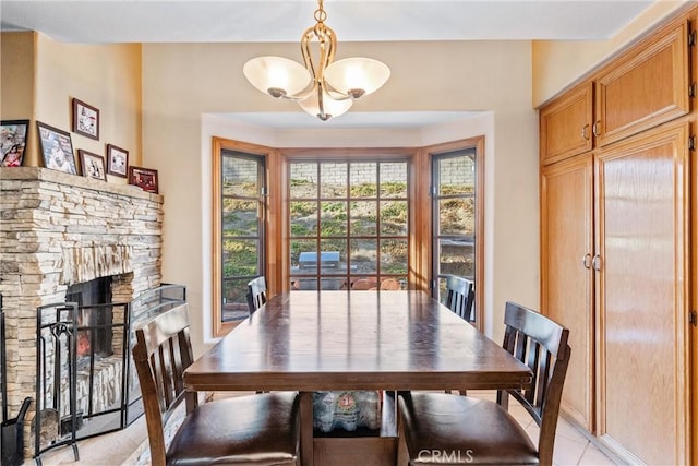 dining area featuring a stone fireplace, a chandelier, and light tile patterned floors