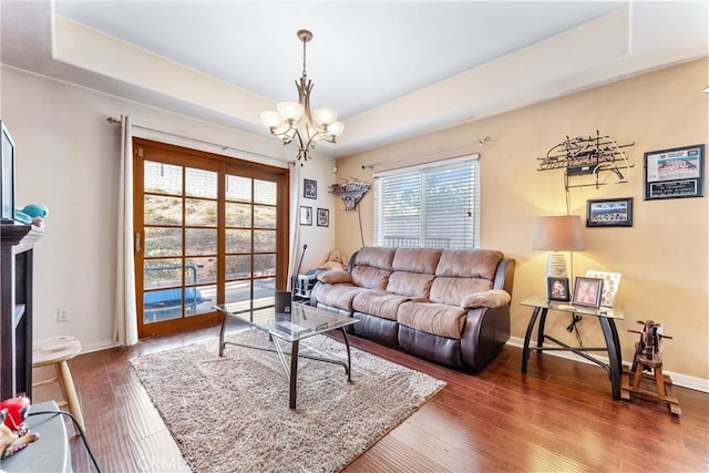 living room with dark wood-type flooring, an inviting chandelier, and a tray ceiling