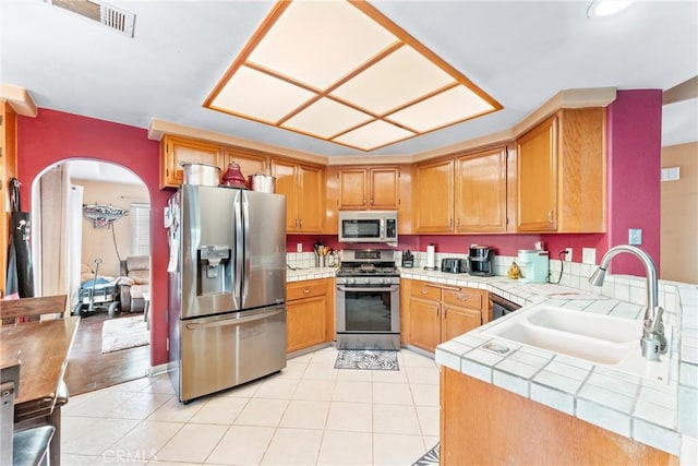 kitchen featuring kitchen peninsula, tile counters, stainless steel appliances, light tile patterned flooring, and sink