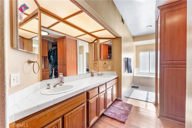 bathroom with tiled bath, wood-type flooring, and vanity