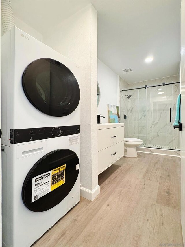 bathroom with wood-type flooring, a shower with door, vanity, toilet, and stacked washing maching and dryer