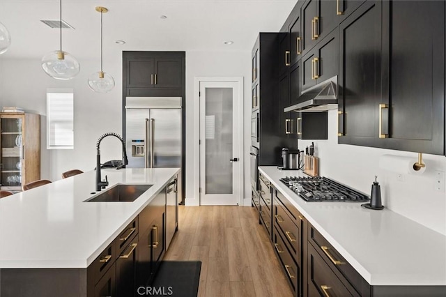 kitchen with appliances with stainless steel finishes, pendant lighting, a center island with sink, and sink