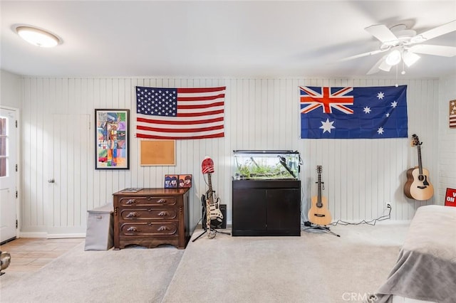 bedroom with carpet flooring, ceiling fan, and wooden walls