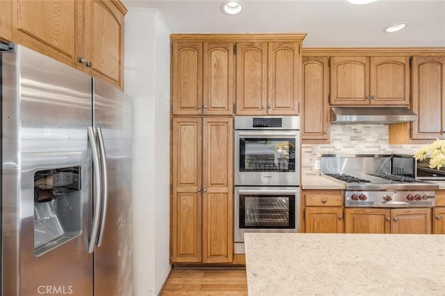 kitchen with backsplash, light stone countertops, stainless steel appliances, and light hardwood / wood-style flooring