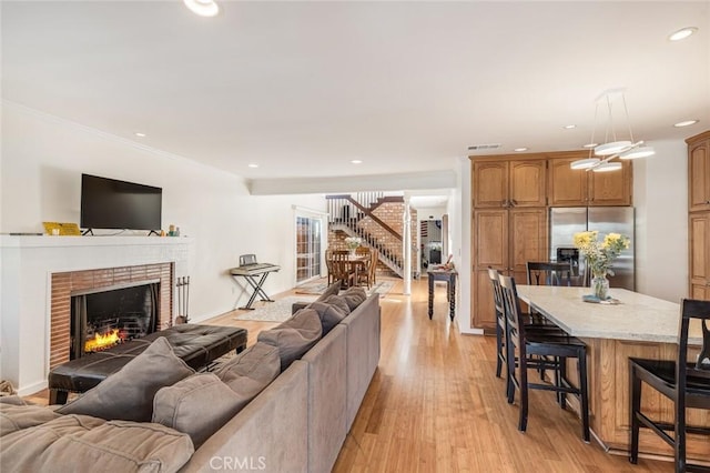 living room with light wood-type flooring, a brick fireplace, and ornamental molding