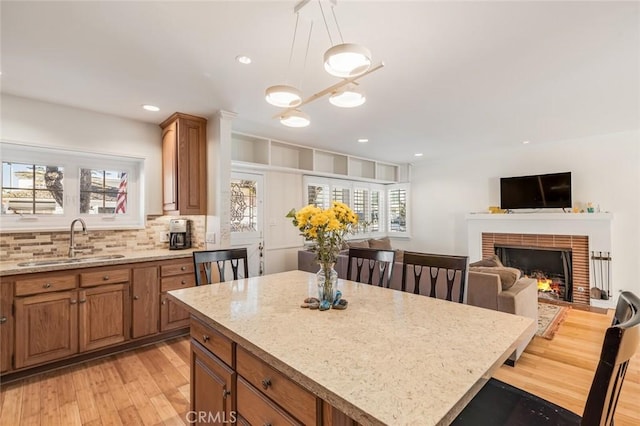 kitchen with light stone countertops, sink, a brick fireplace, decorative light fixtures, and a kitchen island