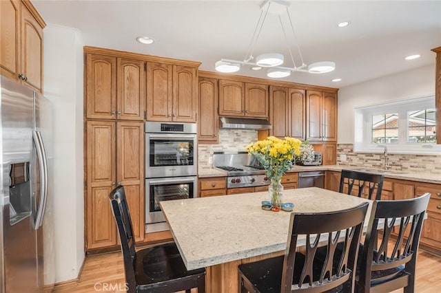 kitchen with sink, decorative backsplash, appliances with stainless steel finishes, a kitchen island, and a kitchen bar