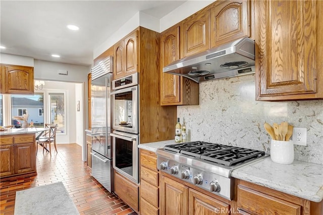 kitchen featuring light stone counters, backsplash, appliances with stainless steel finishes, and exhaust hood