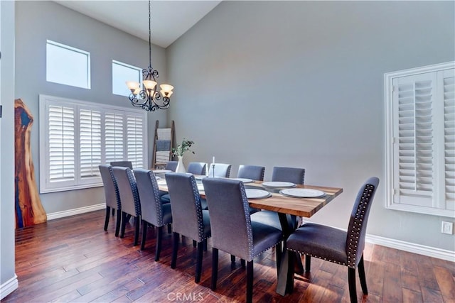 dining space featuring dark wood-type flooring, a towering ceiling, and a notable chandelier