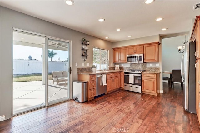 kitchen with light stone countertops, appliances with stainless steel finishes, dark wood-type flooring, sink, and backsplash