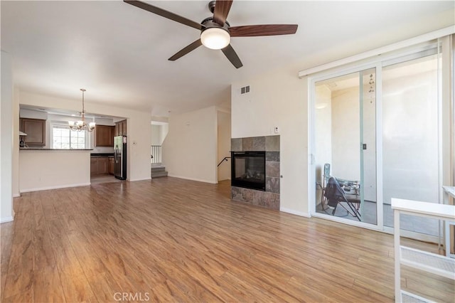 unfurnished living room featuring light wood-type flooring, ceiling fan with notable chandelier, and a fireplace