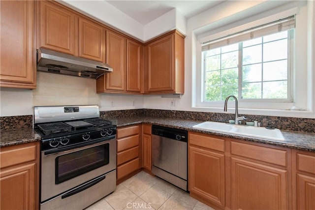 kitchen with exhaust hood, sink, light tile patterned flooring, stainless steel appliances, and dark stone counters