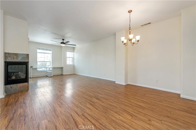 unfurnished living room featuring hardwood / wood-style floors, ceiling fan with notable chandelier, and a tiled fireplace