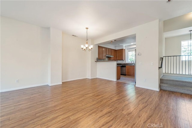 unfurnished living room with a notable chandelier, sink, and light hardwood / wood-style flooring