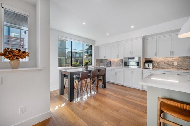 kitchen featuring tasteful backsplash, white cabinets, oven, and light hardwood / wood-style floors