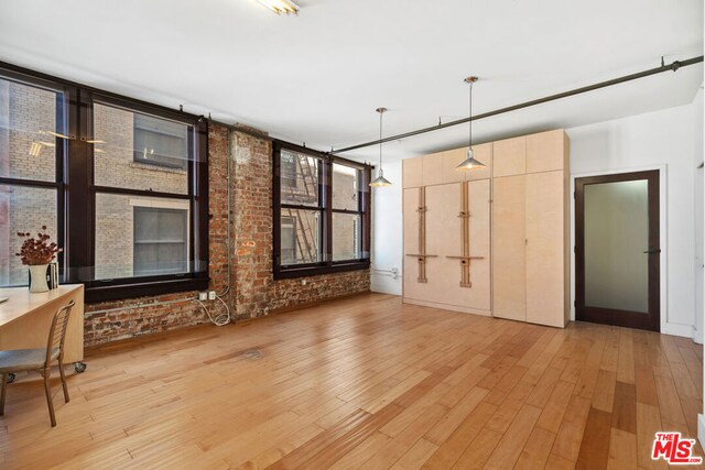 unfurnished living room with a brick fireplace, brick wall, and light hardwood / wood-style flooring