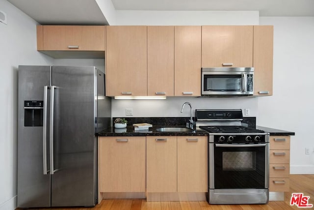 kitchen featuring sink, light hardwood / wood-style flooring, appliances with stainless steel finishes, light brown cabinets, and dark stone counters